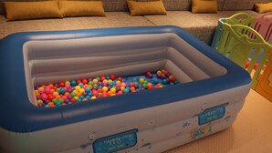 A baby playpen with colorful plastic balls inside, placed in a living room with a couch and cushions in the background. - Holiday Inn Tianjin Wuqing (Tianjin)