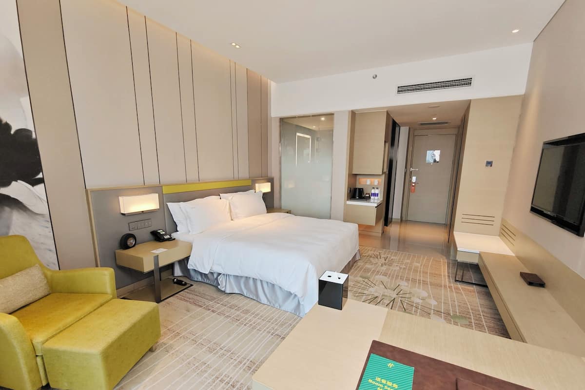 A modern hotel room with a large bed, a desk, a chair, a TV, and a bathroom visible through an open door.