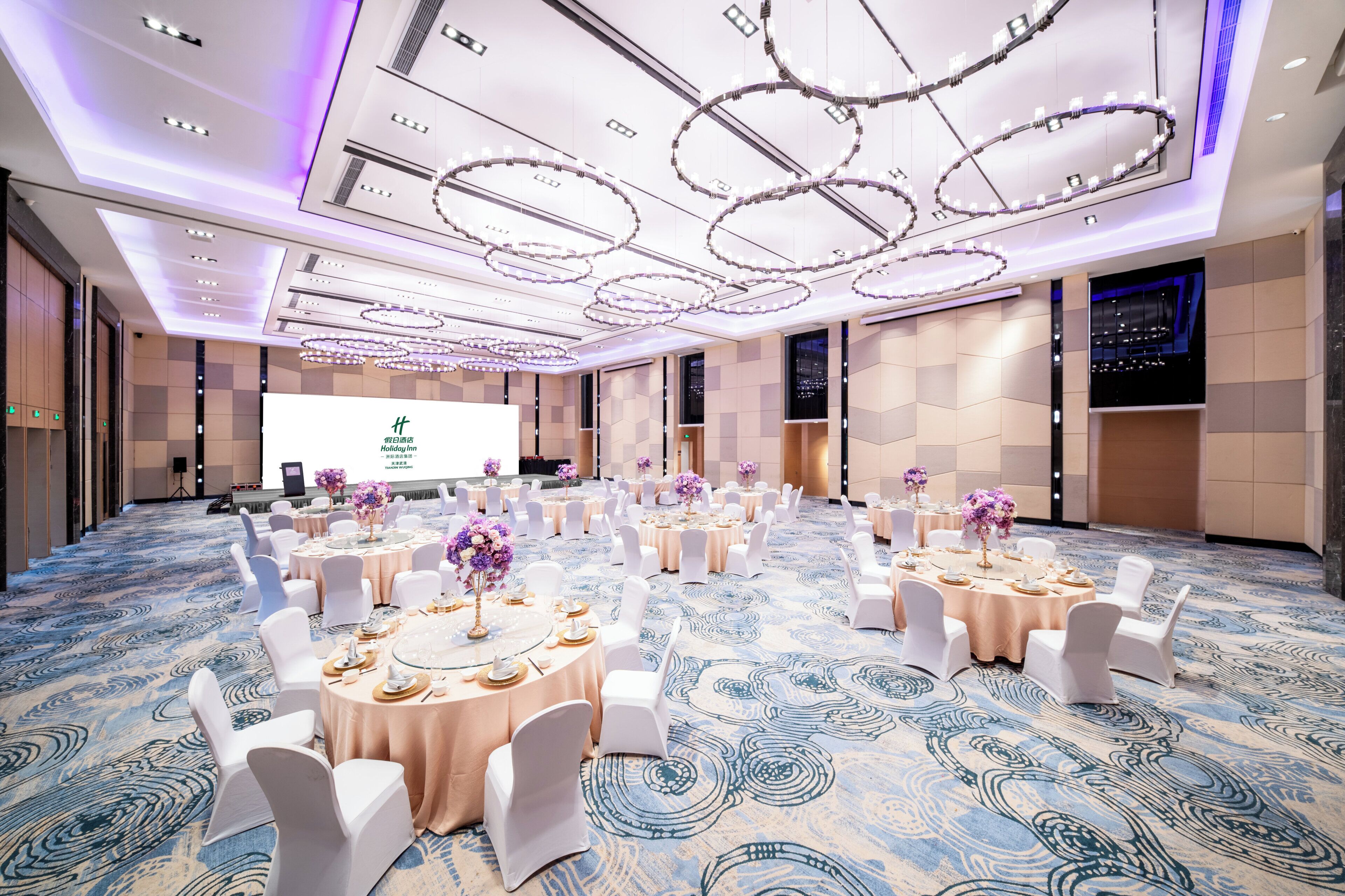 A conference room with round tables, white chairs, and floral centerpieces.