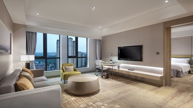 A modern hotel room with a large window, a flat-screen TV, a sofa, a desk, and a bed. - Holiday Inn Tianjin Wuqing (Tianjin)