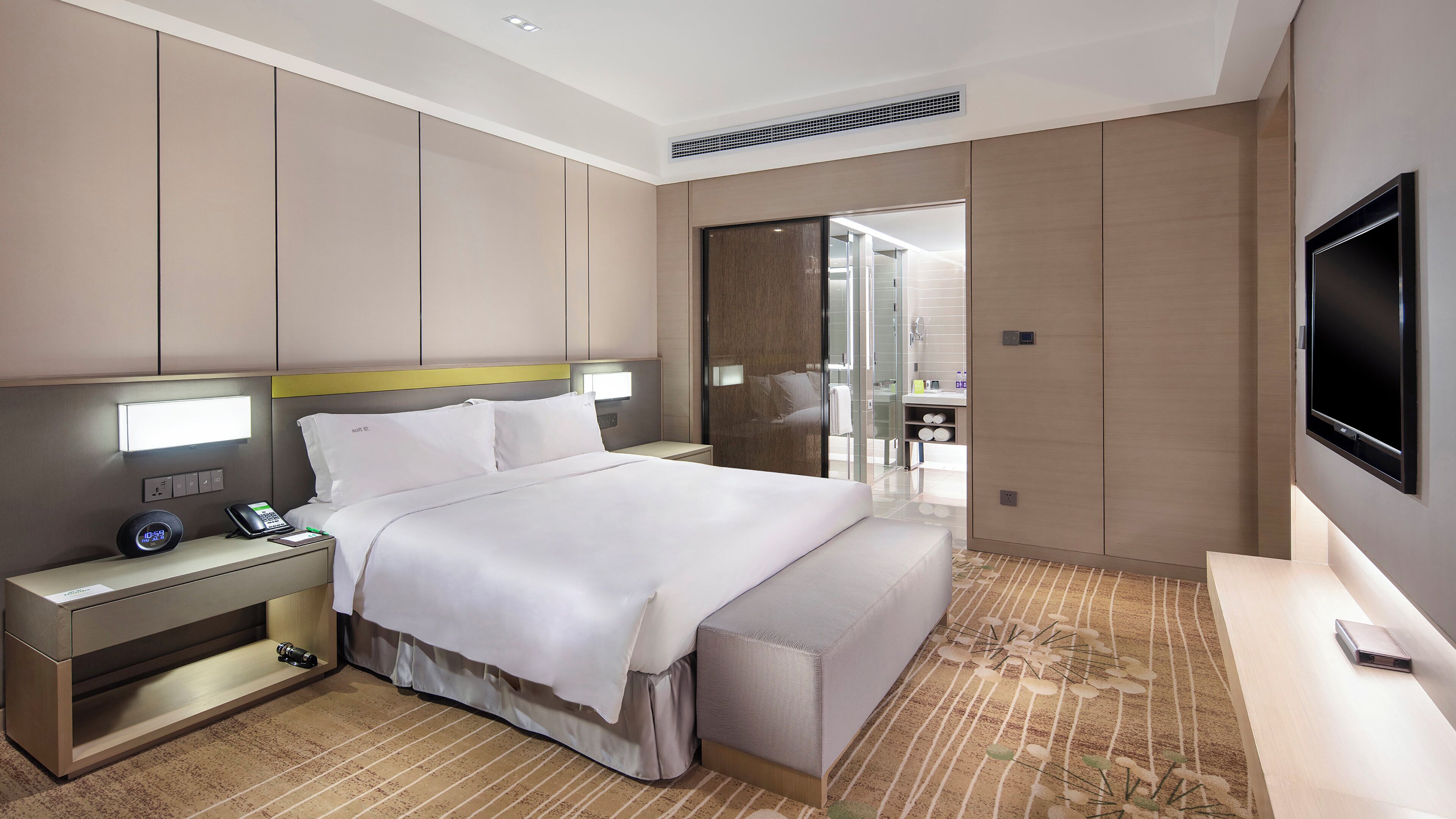 A modern hotel room with a bed, bedside table, lamp, and a TV.