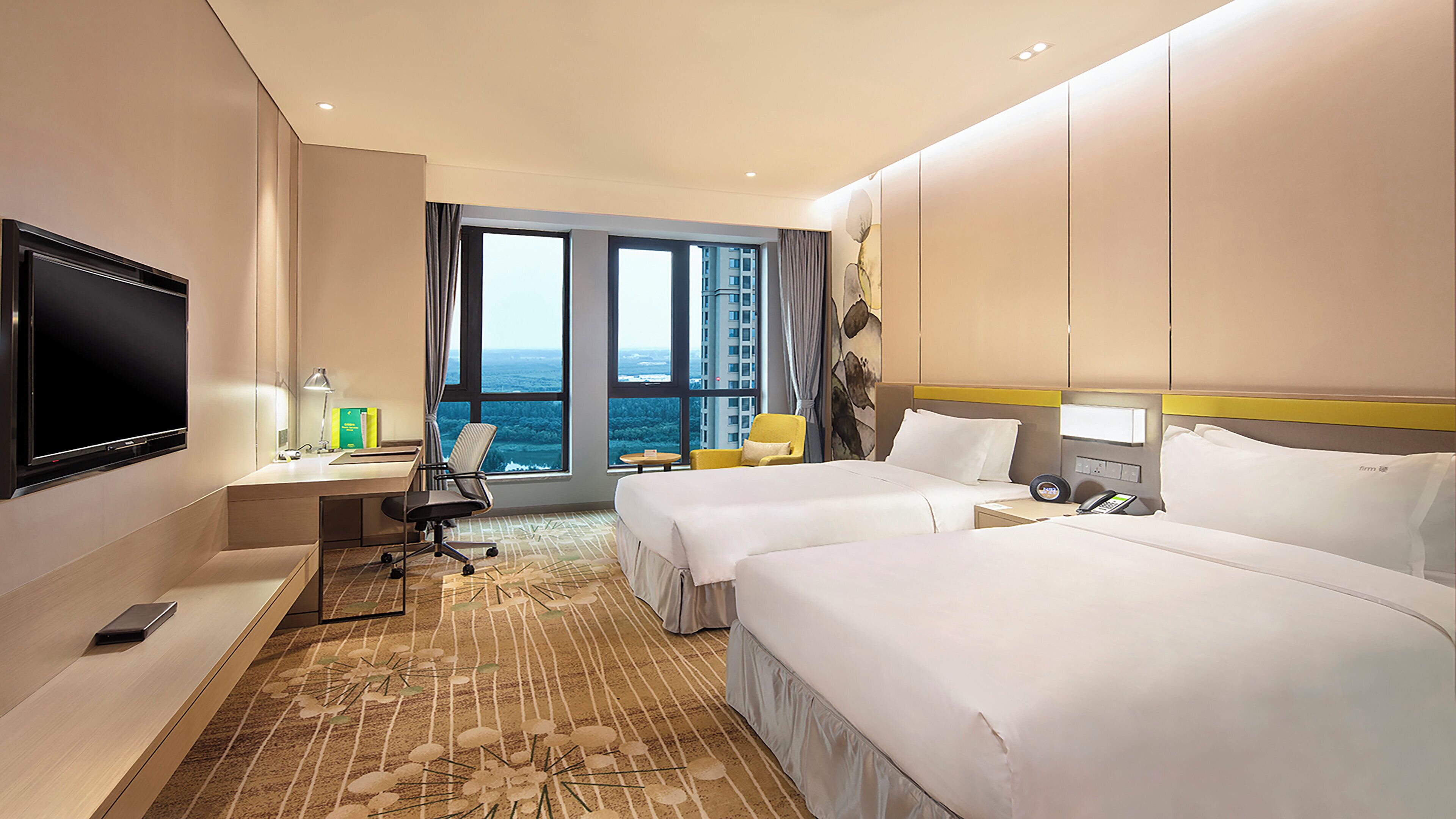 Habitación de hotel con televisor grande, escritorio con lámpara, dos camas, una silla y vistas a la ciudad.