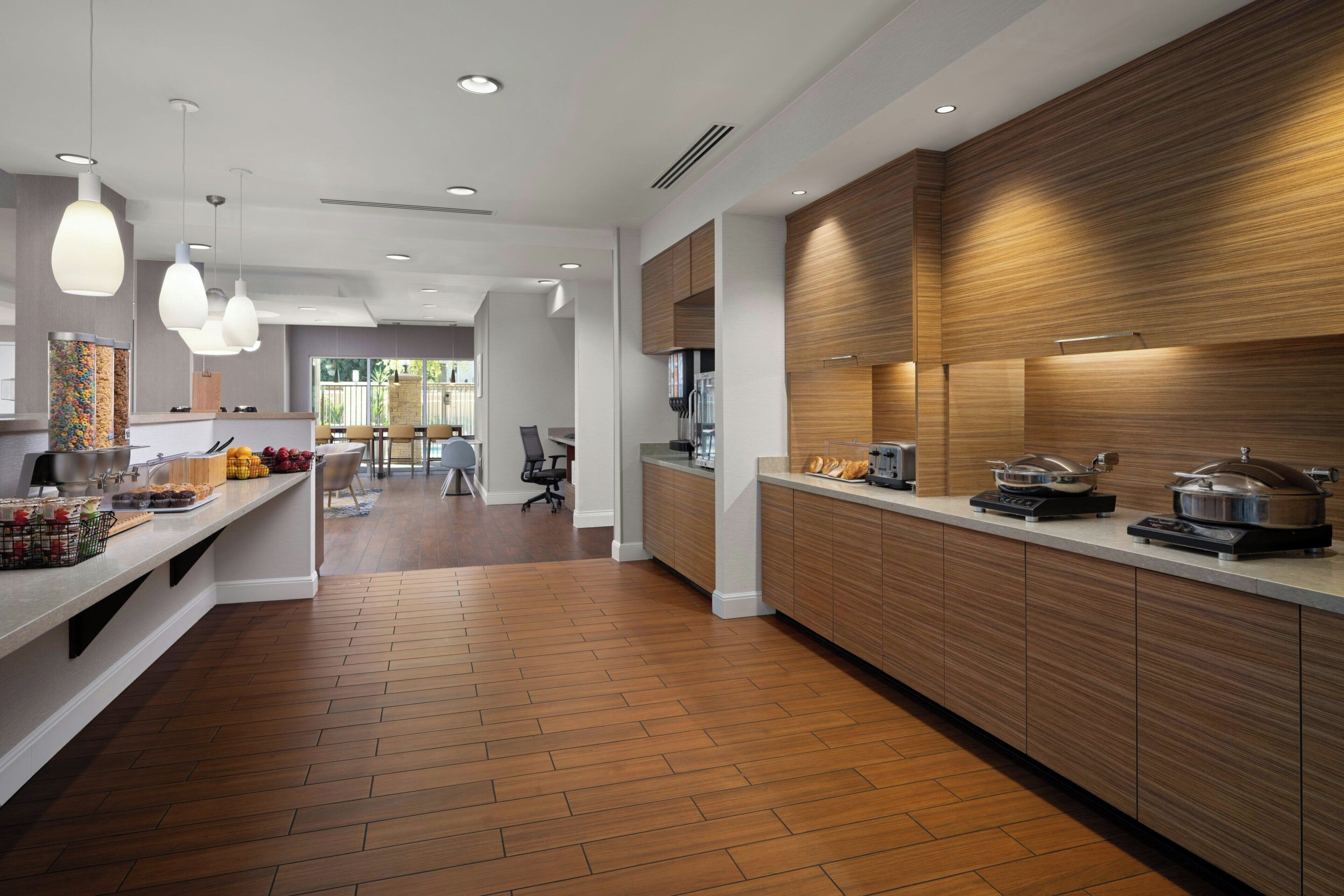 A modern kitchen with wooden cabinets, a long countertop, and pendant lighting.