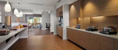 A modern kitchen with wooden cabinets, a long countertop, and pendant lighting.
