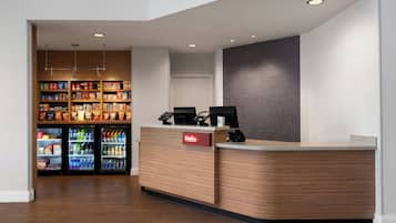 A reception area with a wooden reception desk, a 'Hello' sign, and a wall-mounted screen. There are refrigerated beverage dispensers in the background.