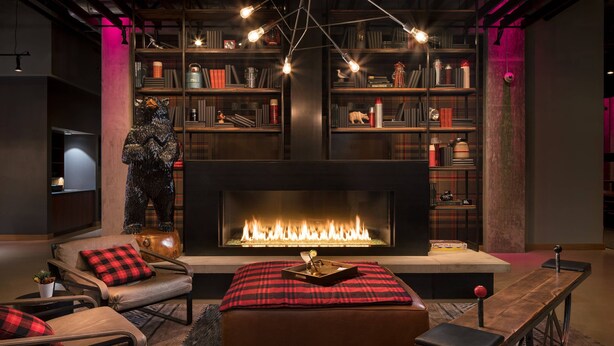 A cozy living room with a fireplace, leather sofas, and a bookshelf filled with books and decorative items. - MOXY Seattle Downtown (Seattle)