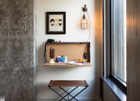 A compact workspace with a corkboard, a small shelf with personal items, a desk lamp, and a window with a view.