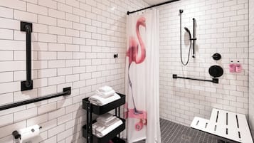Un baño moderno con paredes de azulejos blancos, una ducha con cortina de flamencos rosados, un asidero negro y un estante con toallas.