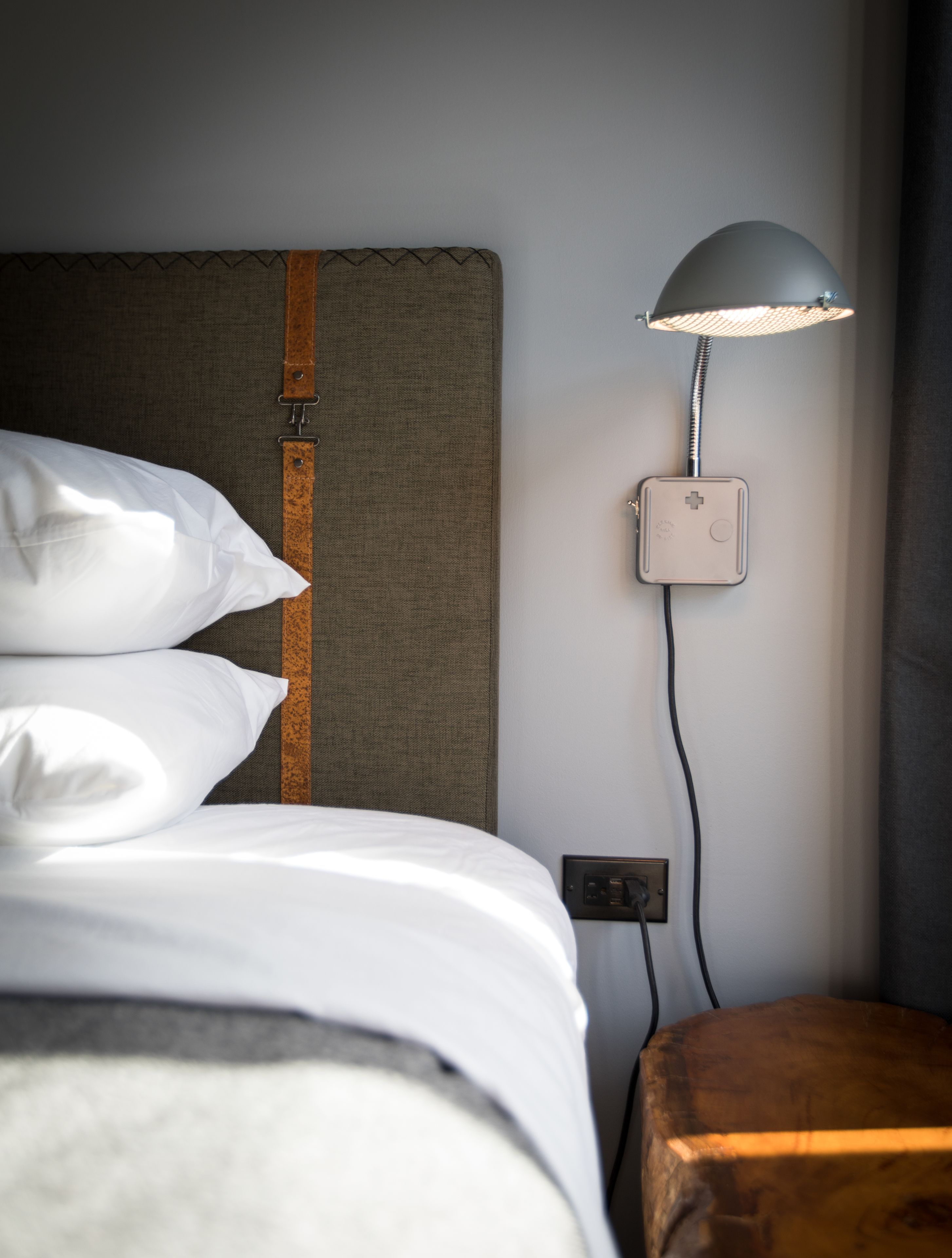 A neatly made bed with white linens, a headboard with a leather accent, and a bedside table with a lamp.