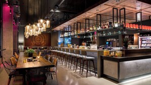 A modern bar area with a long counter, multiple stools, and a variety of bottles and glasses. - MOXY Seattle Downtown (Seattle)