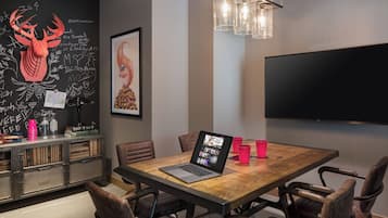 Un salón de conferencias con una mesa de madera, sillas de cuero, una computadora portátil y un televisor de pantalla plana grande.
