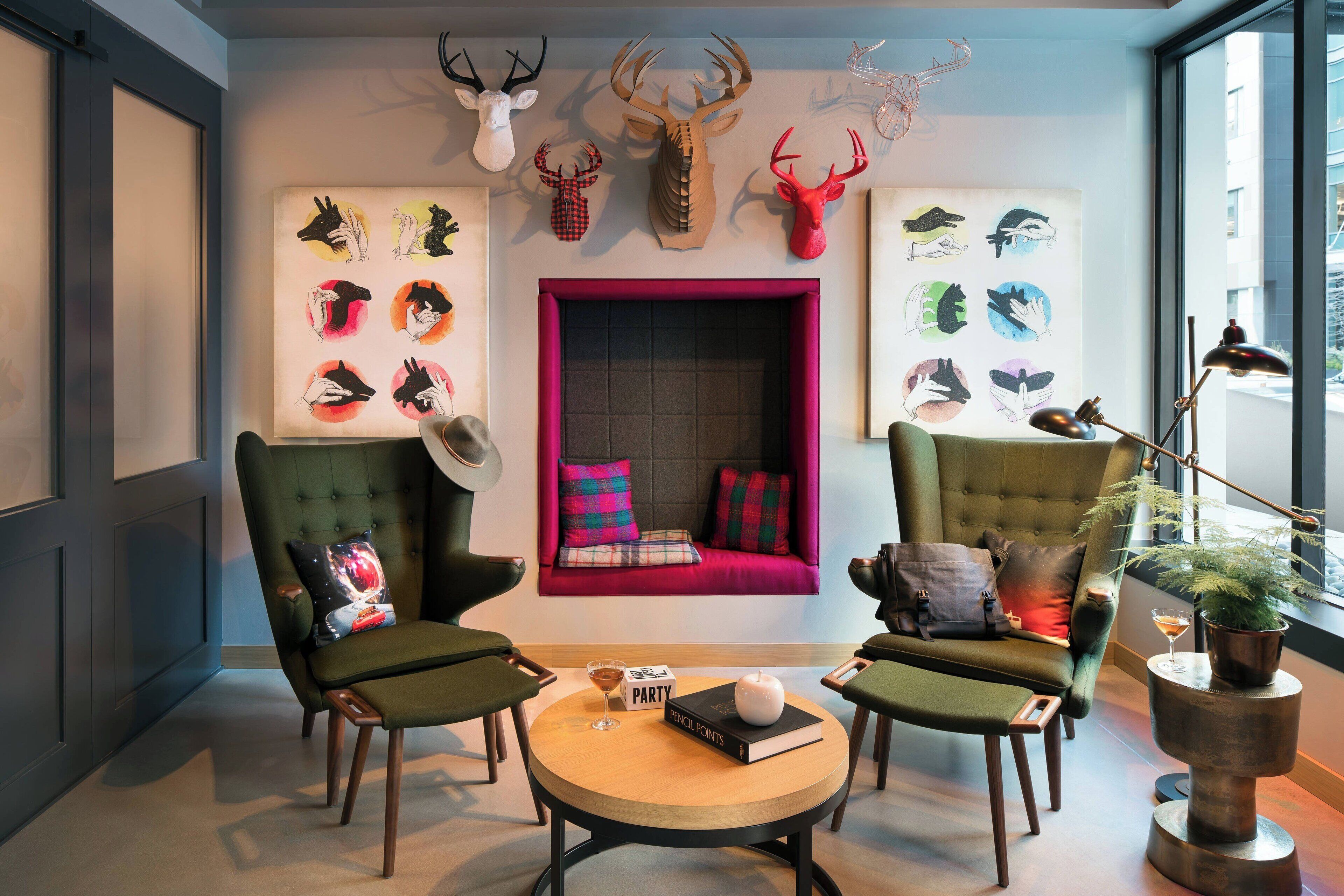 A modern living room with two green armchairs, a round coffee table, and a fireplace with colorful cushions.
