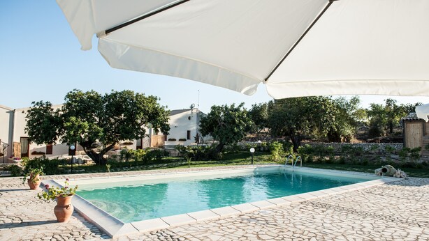 A swimming pool with a tiled deck, surrounded by potted plants and a large umbrella. - farmhouse I 5 SENSI (Vr) (modica)