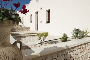 A white building with a stone pathway leading to the entrance, small potted plants, and a stone wall.