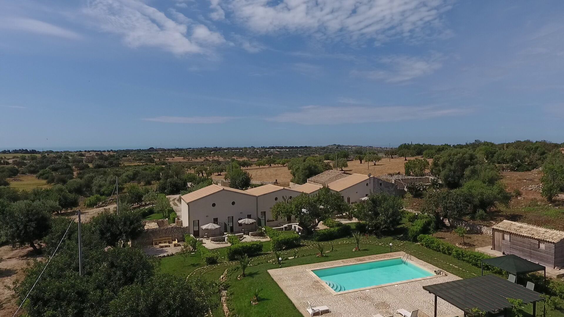 A residential area with a swimming pool, multiple houses, and a clear view of the surrounding landscape.