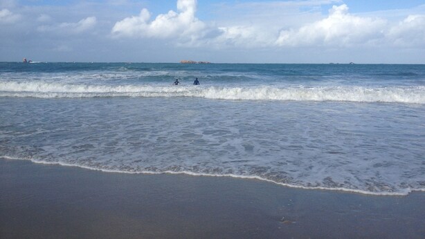Una playa con olas, cielo despejado y formas de tierra en la distancia.
