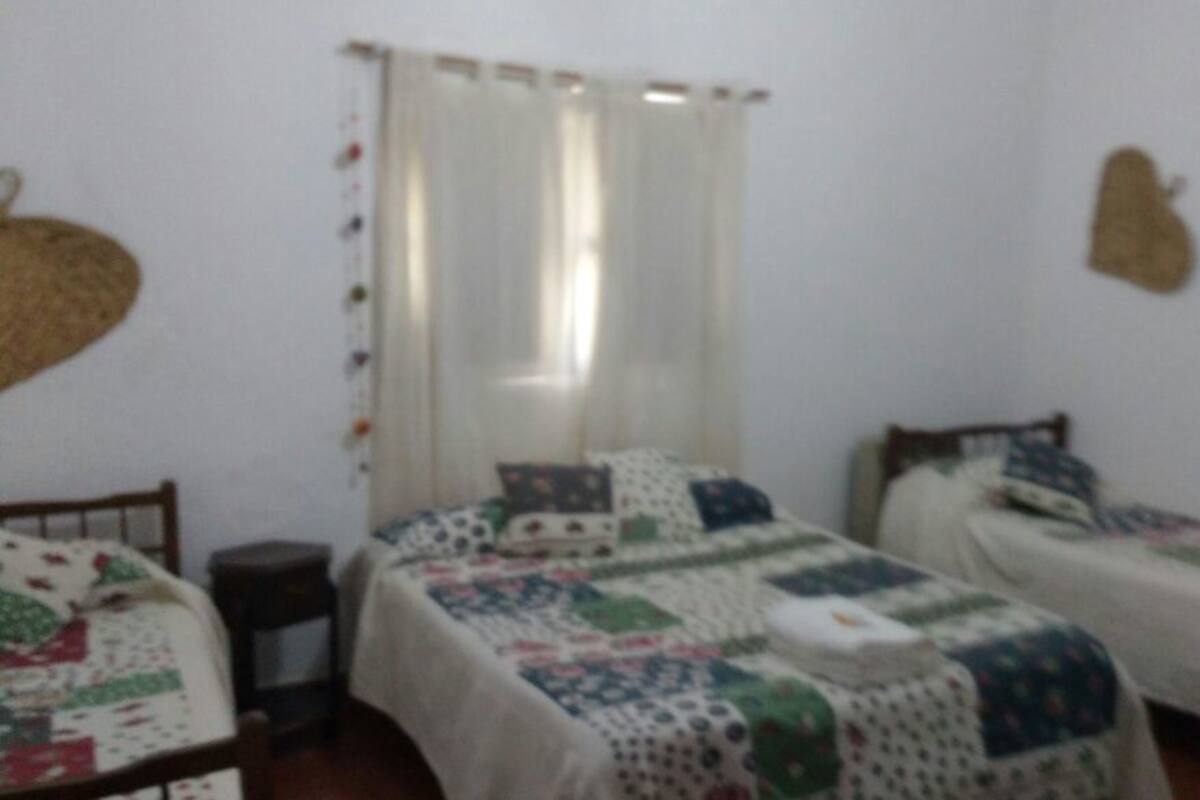 A small, simple room with two single beds, a nightstand, and a window with curtains.