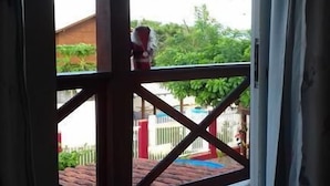 Vista desde un balcón con suelo de baldosas, baranda de metal y un vistazo a un edificio y follaje.