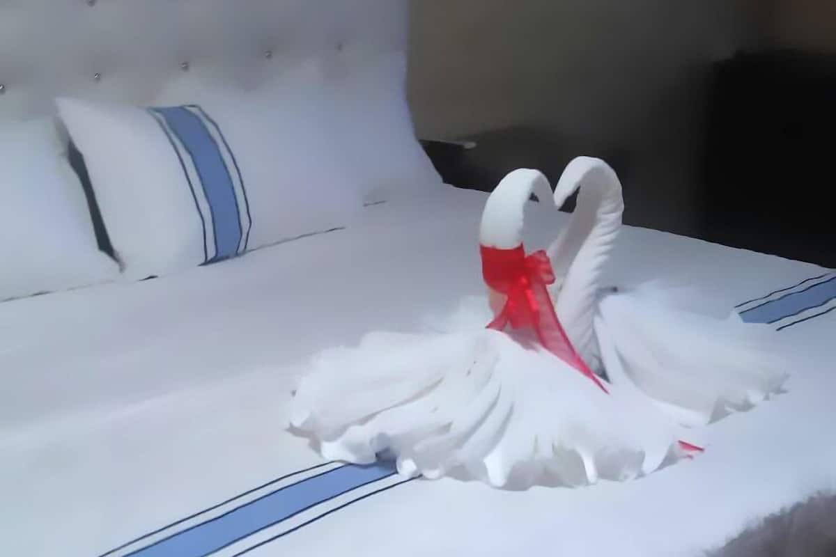 A bed with a white headboard and blue stripes, a white pillow, and a decorative swan made of fabric.