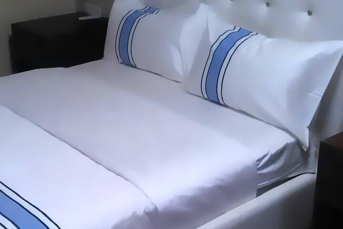 A neatly made bed with white bedding and blue stripes, a tufted headboard, and a nightstand with a lamp.