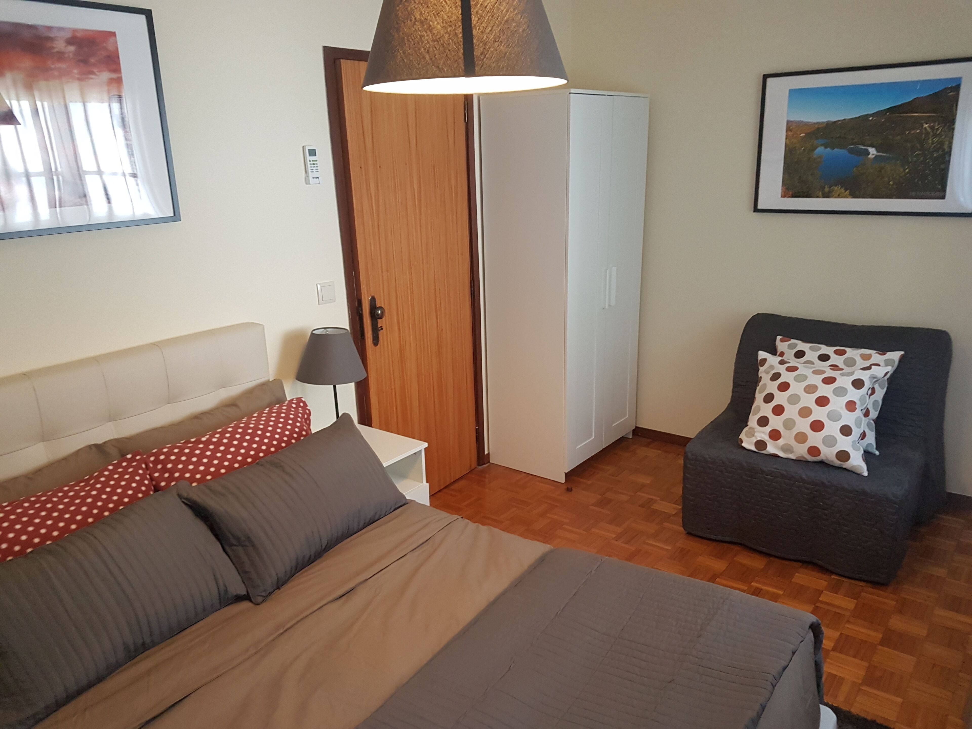 A bedroom with a bed, a chair, a wardrobe, and a lamp.