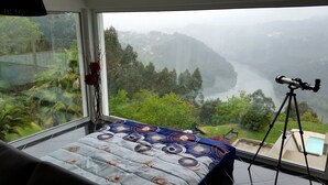 Ein Schlafzimmer mit großem Fenster und Blick auf ein Tal und einen Fluss.