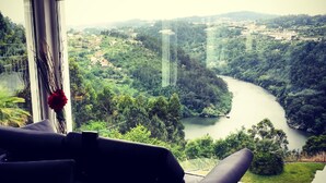 Ein Zimmer mit großem Fenster mit Blick auf einen Fluss und bewaldetes Gebiet.