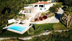 Ein großzügiges Haus mit Schwimmbad, umgeben von üppiger Vegetation und einer steilen Hanglage.