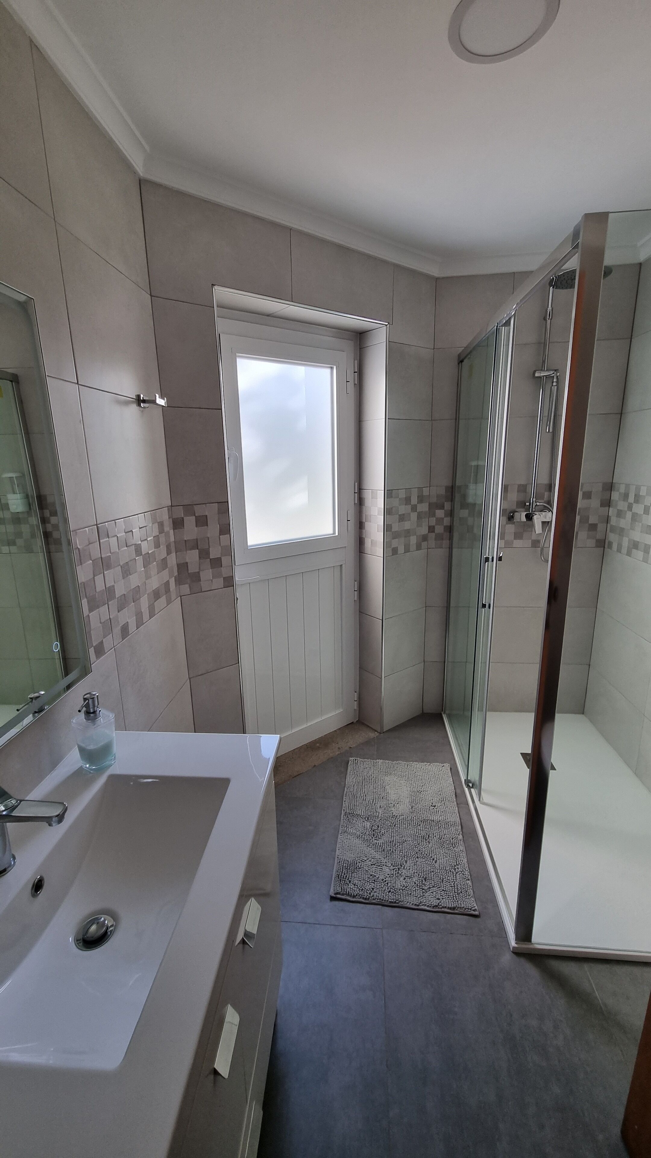 Een moderne badkamer met een ruime wastafel, douche en raam.