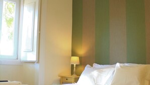Ein ordentlich bezogenes Bett mit einer gestreiften Decke, einer Nachttischlampe und einem Fenster mit Vorhängen.
