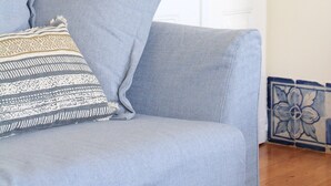 Ein hellblaues Sofa mit einem gemusterten Kissen, eine Stehlampe und eine dekorative Fliese neben einer weißen Tür.