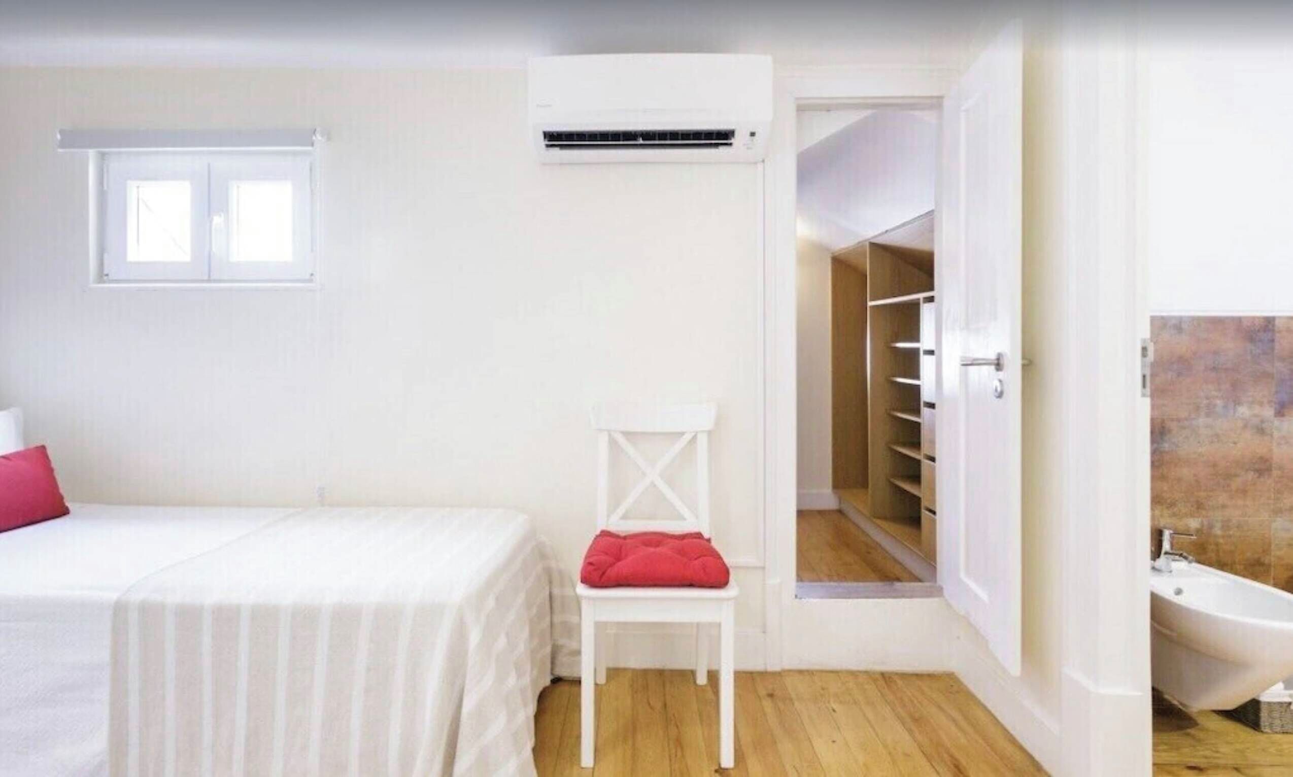 Une chambre à coucher comprenant un lit, une chaise, un appareil de climatisation, une fenêtre et une salle de bain avec une baignoire.