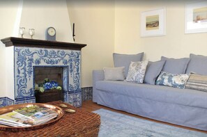 A living room with a blue-tiled fireplace, a grey sofa, and a magazine tray.