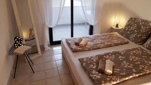 A bedroom with a bed, a bedside table with a lamp, a mirror, and a window with sheer curtains. - Casa Nostra (Funtana)