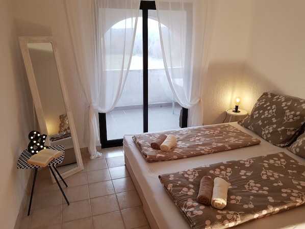 Une chambre à coucher avec un lit, une table de chevet avec une lampe, un miroir et une fenêtre avec des rideaux légers.