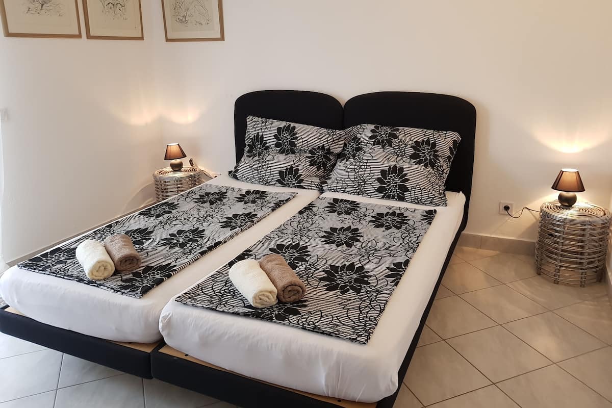 Een tweepersoonsbed met een zwart hoofdbord, twee bedlampjes en een bloemenprintdeken.