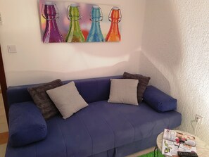 A blue sofa with two pillows, a wall-mounted colorful bottle artwork, and a magazine on a small table.