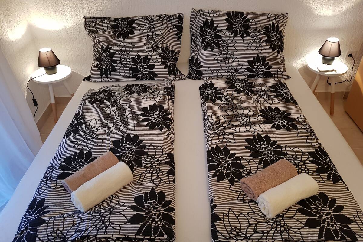 Een tweepersoonsbed met zwart-wit bloemenbeddengoed, twee bedlampjes en een klein tafeltje met een lamp.