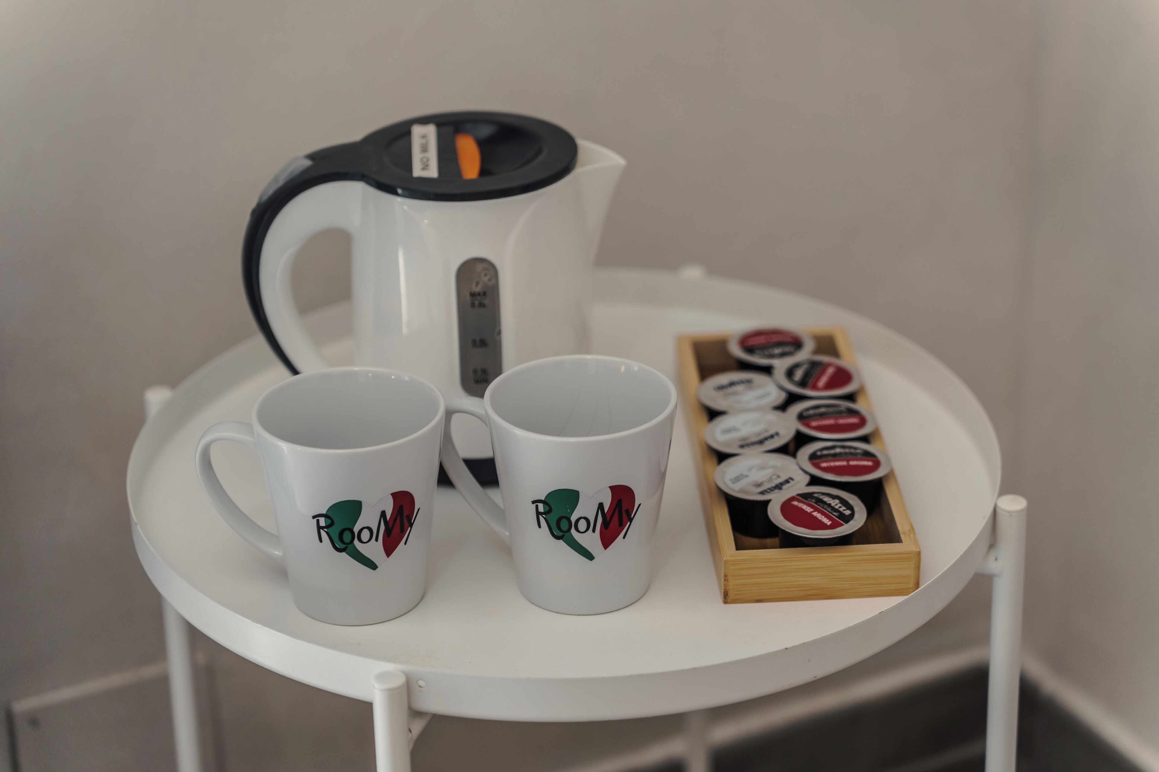 Two white mugs with 'Roomy' text and a coffee maker on a white table.