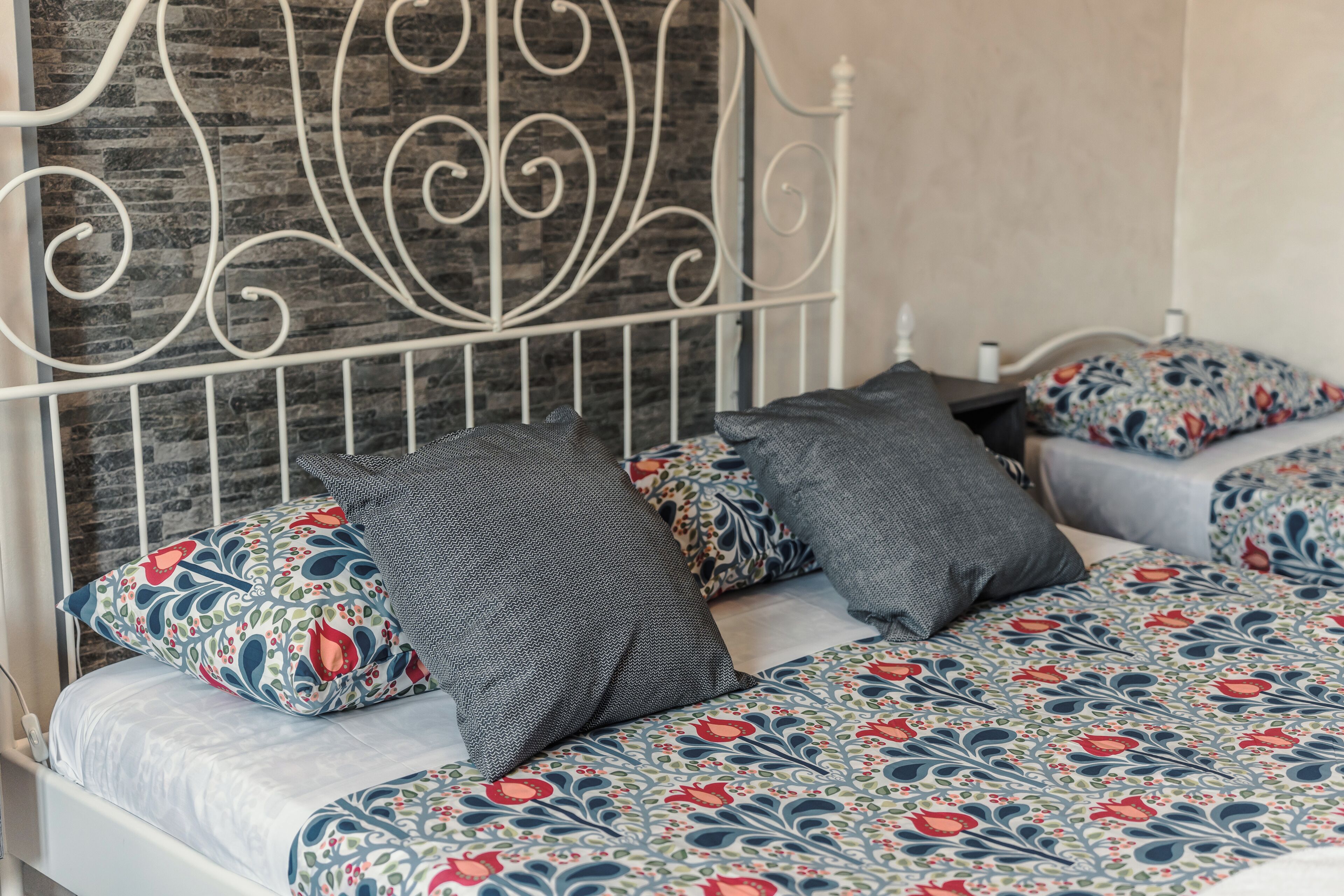 Un lit avec une couvre-lit à motifs, deux oreillers aux dessins différents et une tête de lit en métal.