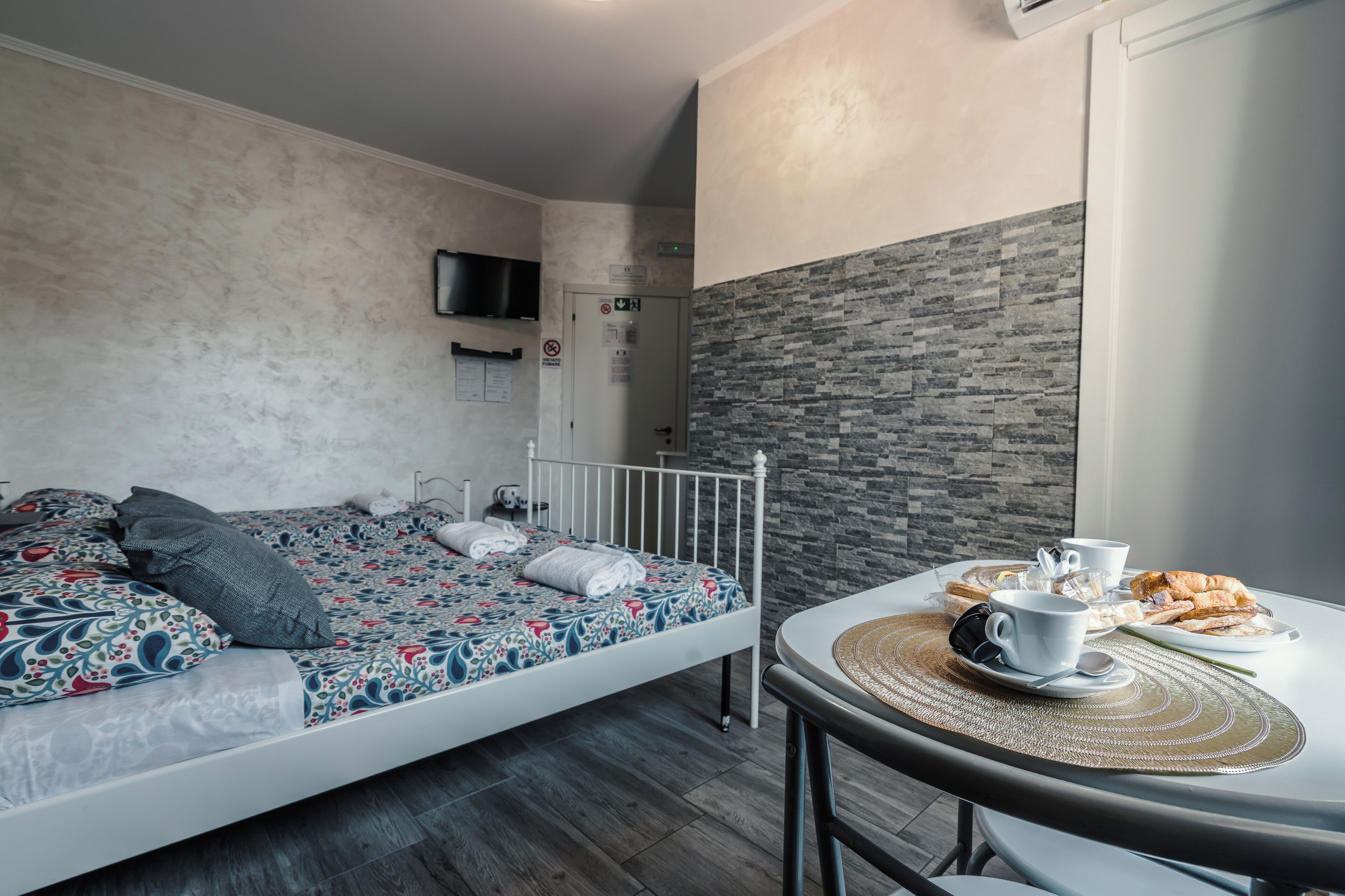 Un dormitorio moderno con cama, televisor montado en la pared y un comedor con mesa lista para el desayuno.