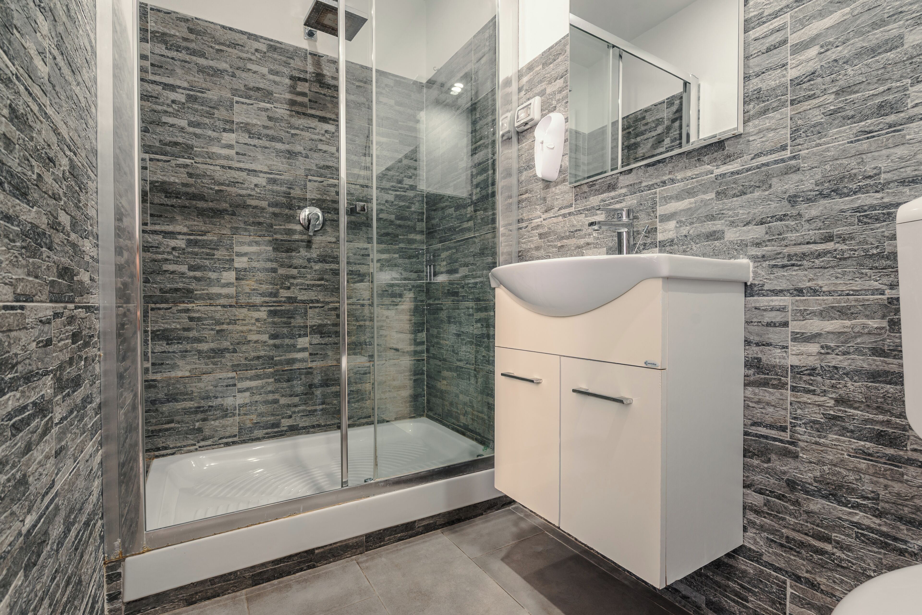 A modern bathroom with a glass-enclosed shower, a white sink, and a mirror above it.