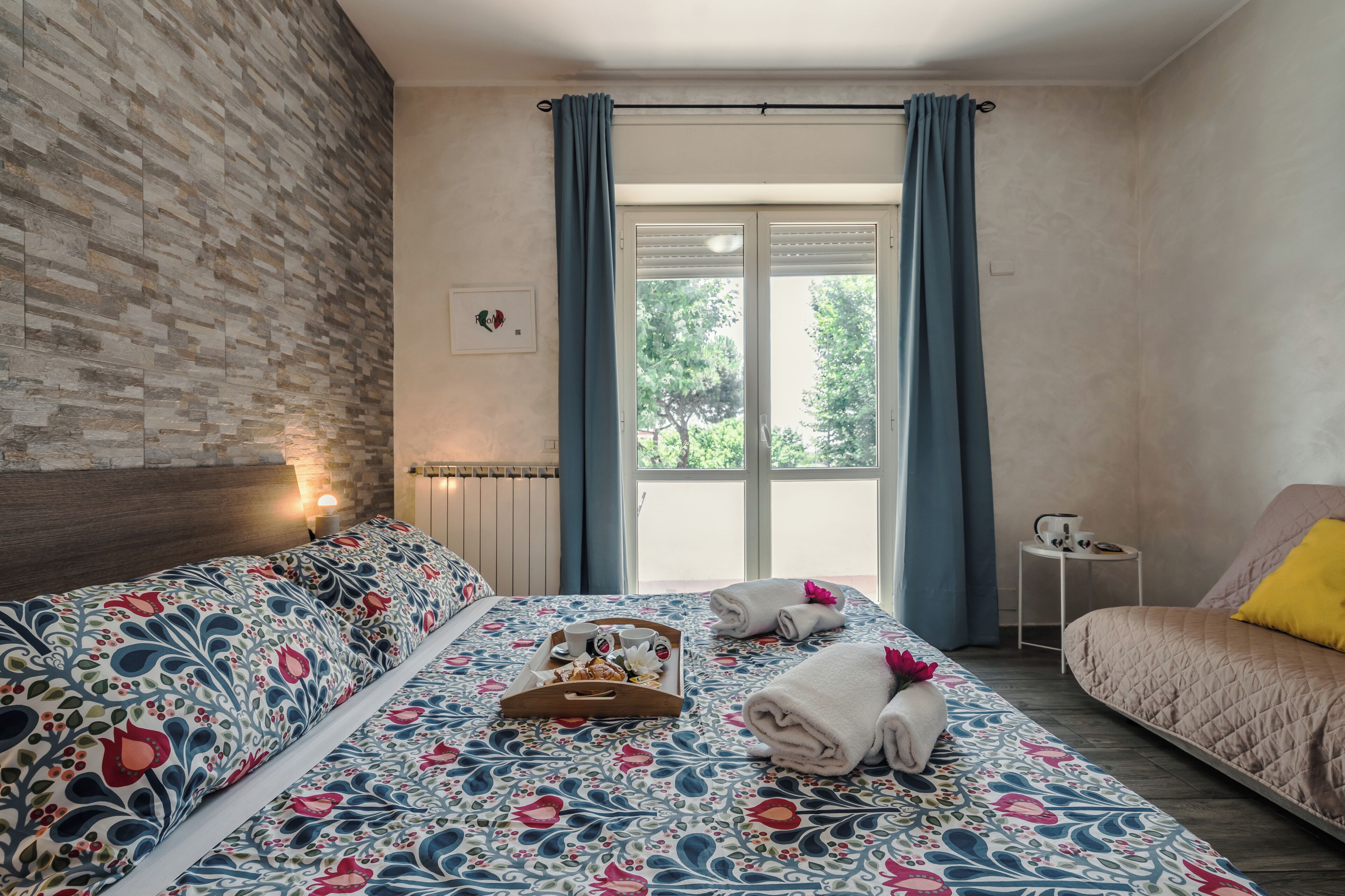 Une chambre d’hôtel avec un lit, un canapé, une petite table et une fenêtre avec des rideaux.