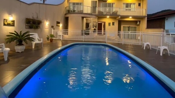 A modern hotel with a swimming pool, multiple balconies, and a well-lit exterior. - Pousada Juliane (Penha)