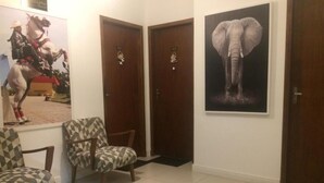 A hallway with two wooden doors, a poster of a horse rider, and a poster of an elephant. There are two patterned chairs in the room. - Pousada Juliane (Penha)