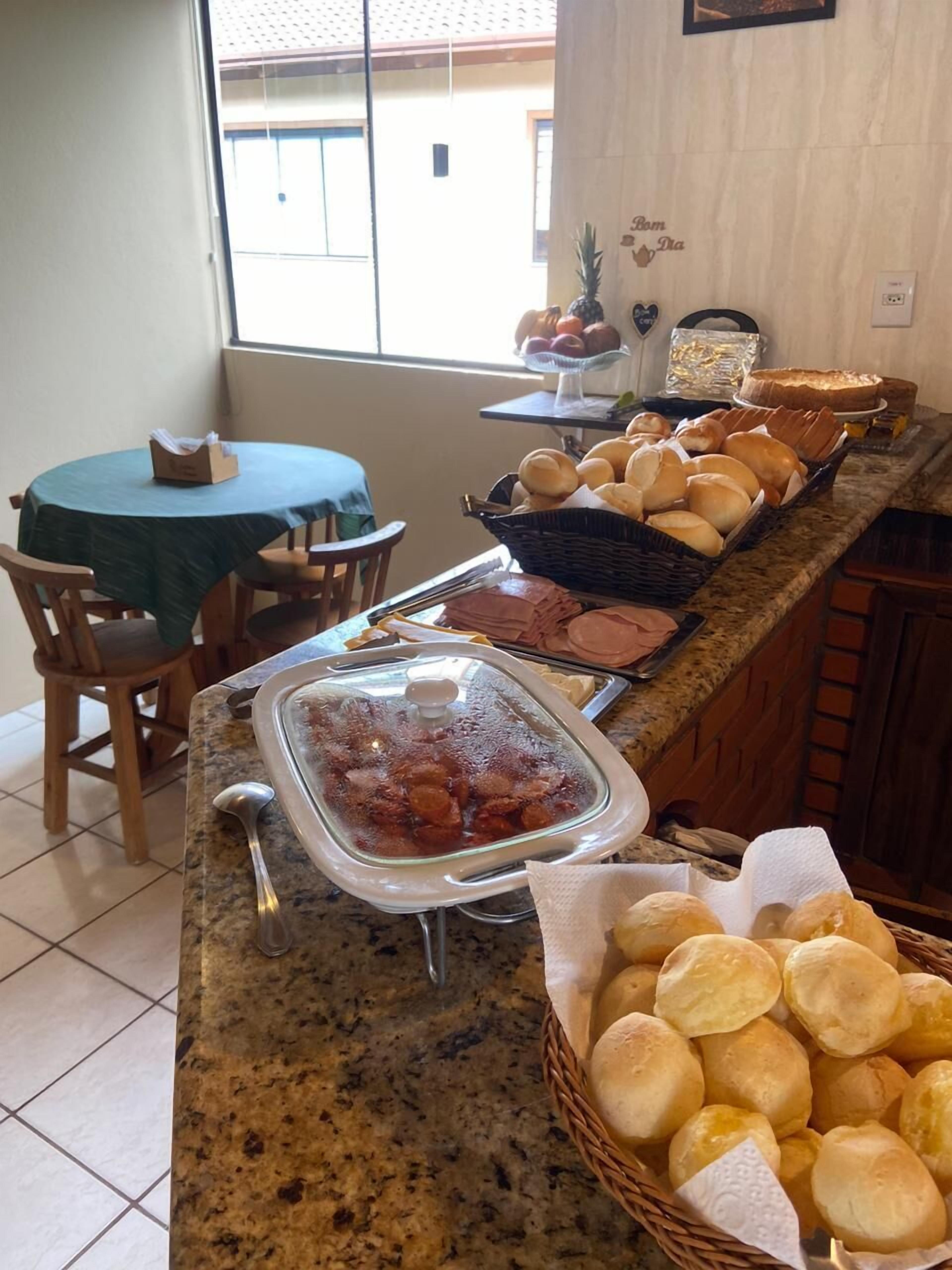 A buffet area with various food items, a covered dish with meat, and a table with chairs.