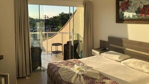 A hotel room with a bed, a desk, a chair, and a balcony with a view of the city. - Pousada Juliane (Penha)