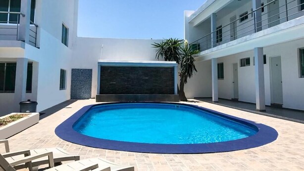 Un edificio moderno con piscina, garaje techado y una palmera.