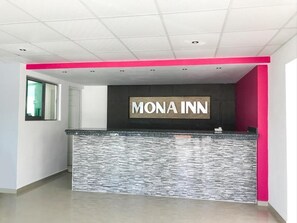 A reception area with a 'MONA INN' sign, a stone-textured counter, and a bright pink accent wall.