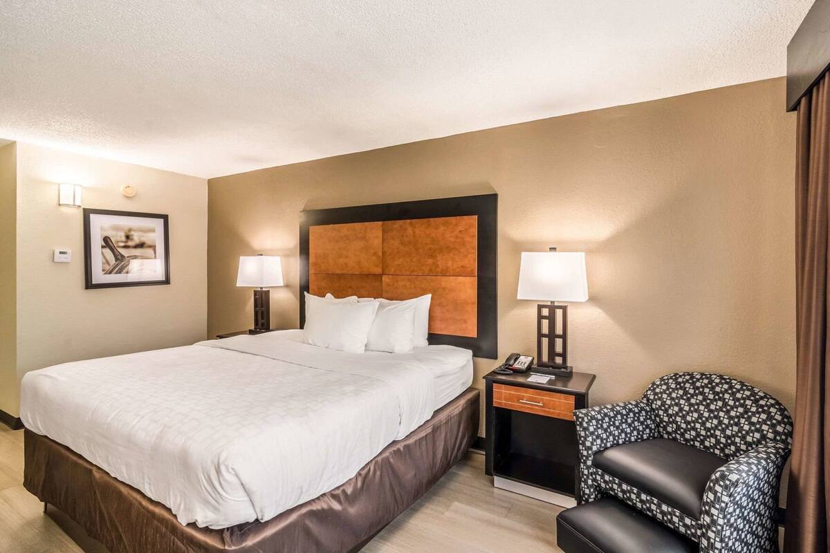 A hotel room with a large bed, two bedside tables with lamps, a chair, and a framed picture on the wall.